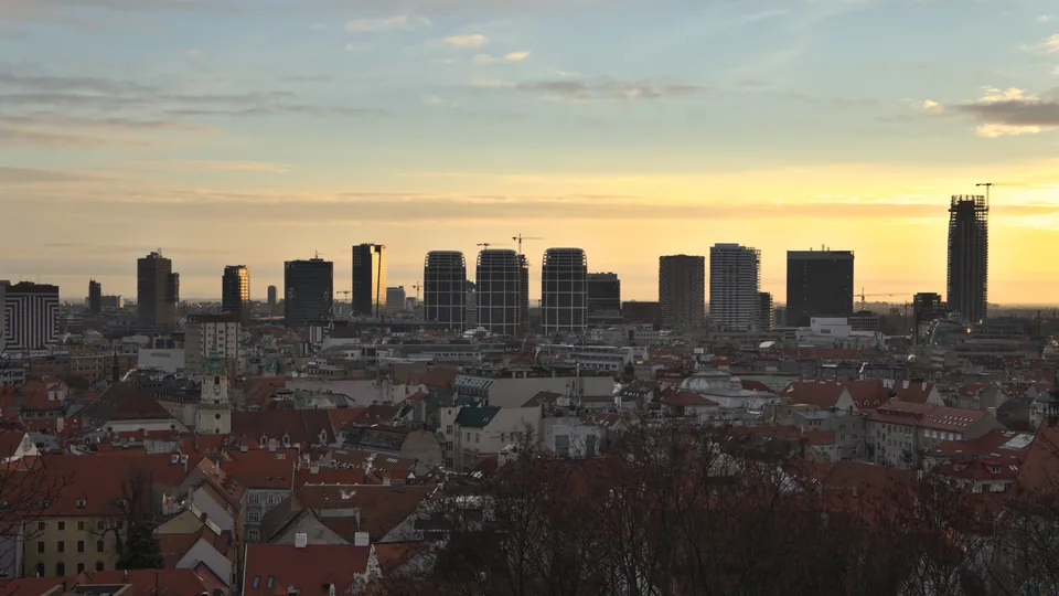 Bratislava's new office and residential towers on the skyline in low winter-morning light, seen over the red roofs of the old town from the castle hill.