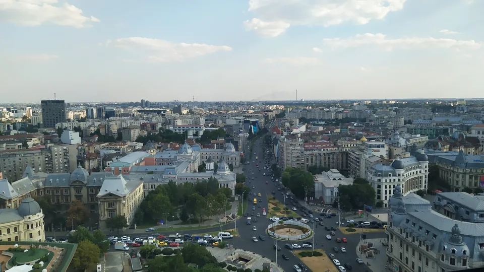Elevated view over central Bucharest on a summer afternoon, a boulevard and roundabout running between historic buildings towards the horizon.
