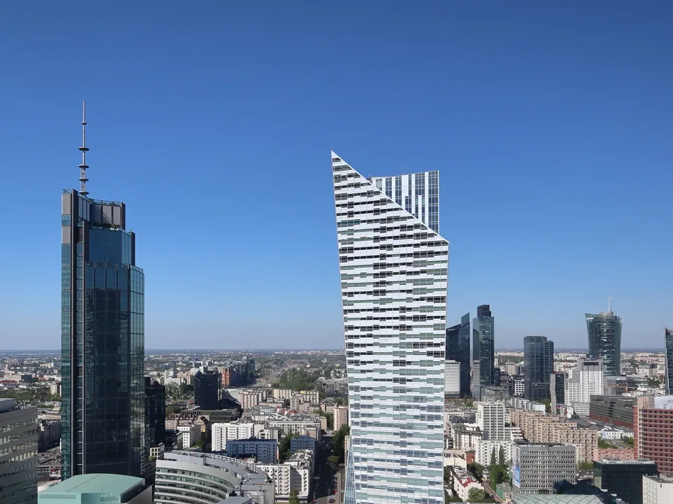 Varso Tower and the Złota 44 residential tower rising over central Warsaw under a clear blue sky, with the Rondo Daszyńskiego office cluster, including Warsaw Spire, on the skyline behind.