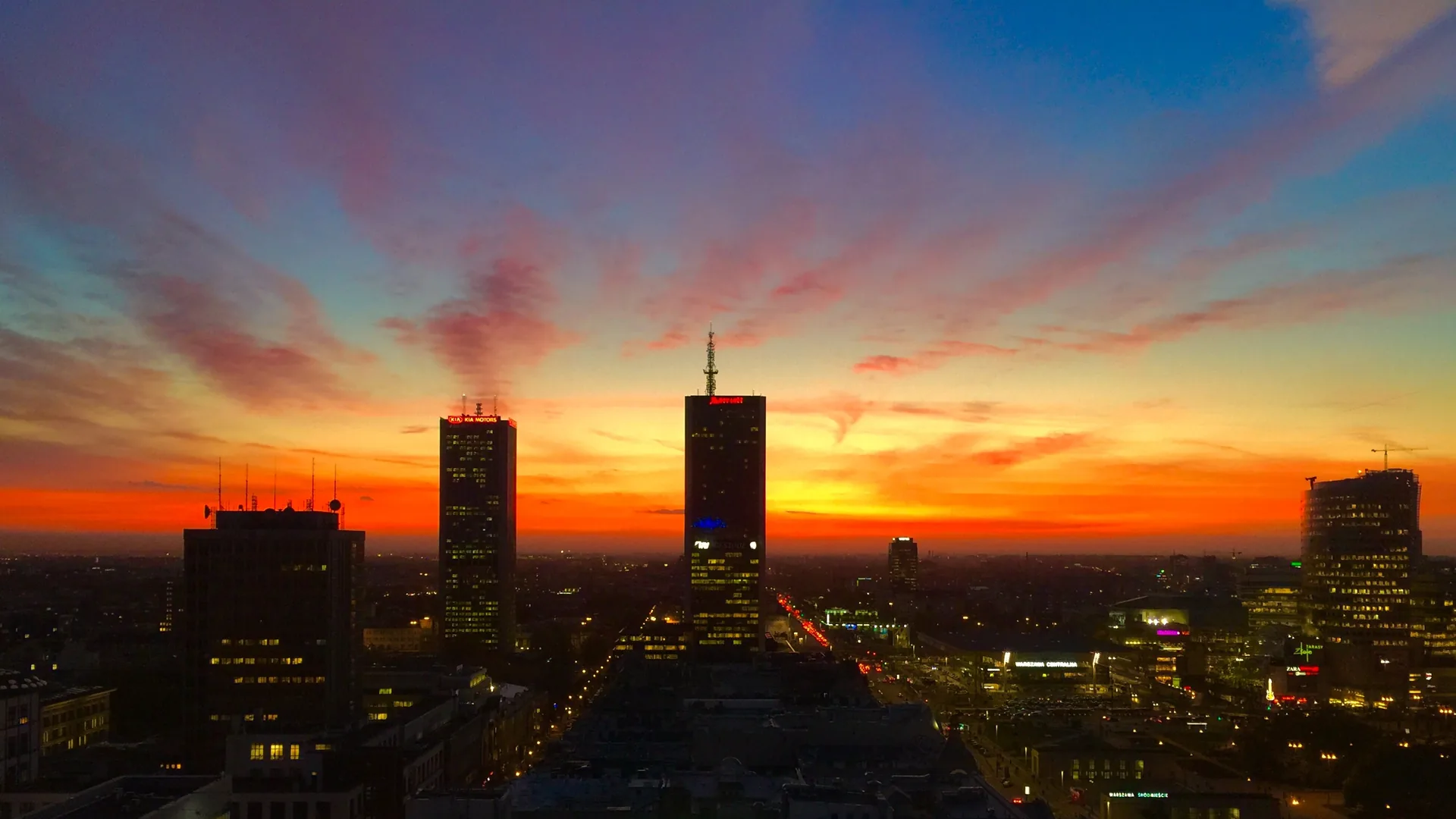 Warsaw city-centre towers in silhouette against a red and orange sky at dusk.