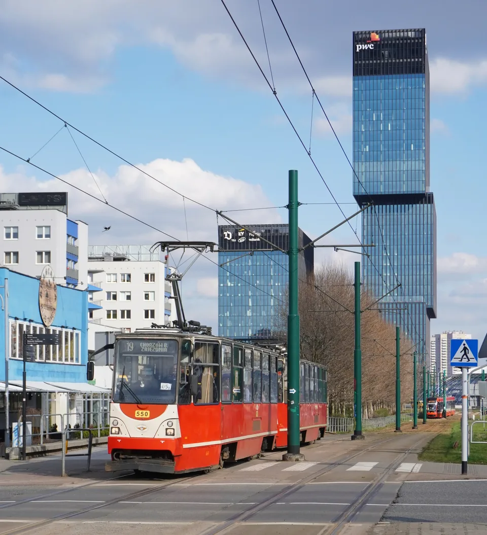 A red tram in central Katowice with glass office towers rising behind it.
