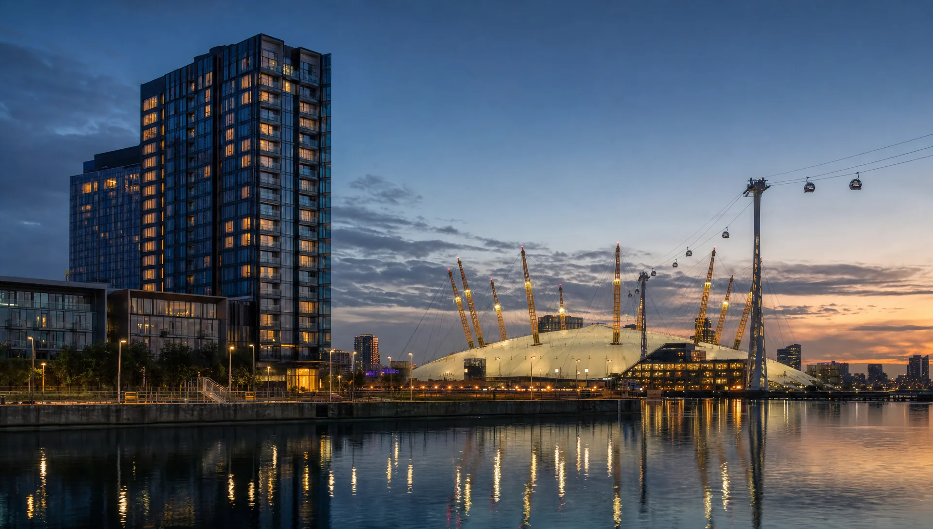 The Greenwich Peninsula waterfront at blue hour, the illuminated O2 dome and cable-car gondolas crossing the Thames.